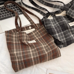 Detail of metal magnetic buckle and woven label on plaid canvas tote bag