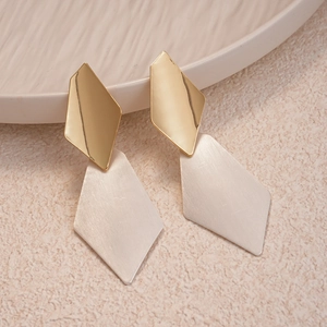 Detail of geometric rhombus drop earrings featuring brushed silver and gold polished finish