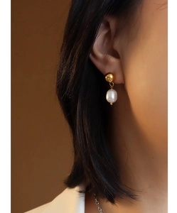 Close-up of elegant gold ball stud earrings with white teardrop pearls worn by a model
