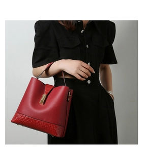 Detail of red bucket bag with crocodile texture and gold buckle on a model