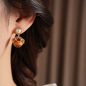 Close-up of vintage golden earrings with white pearl and brown tiger eye stone on model