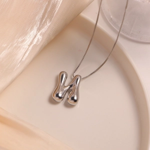 Minimalist silver H-letter pendant necklace with liquid metal finish on silk backdrop