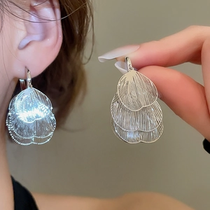 Détail des boucles d'oreilles à pétales creux superposés en argent portées par un modèle