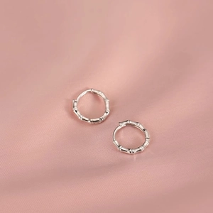 Elegant silver bamboo joint hoop earrings on smooth pink silk background fabric