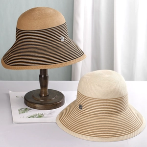 Detail of high-density woven straw hats with striped patterns and square metal logo