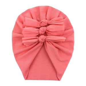 Detail of coral pink baby turban hat featuring triple-layered bows and soft cotton fabric