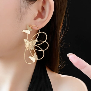 Macro detail of large golden hollow butterfly earrings on a model with a black background