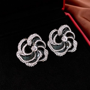 Macro detail of enamel camellia earrings with sparkling crystals on black velvet