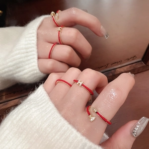 Close-up of red braided rope rings with gold H-letter and nail design on model's hand