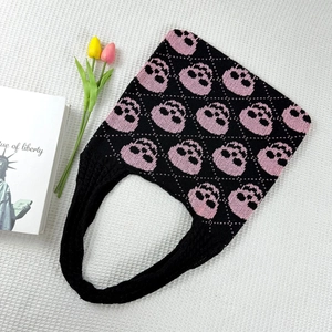 Detail of knitted tote bag featuring pink skull patterns on a black woven fabric