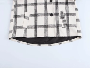 Close-up of black and white plaid jacket hem with button and pocket detail