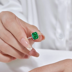Close-up of a square emerald-cut green gemstone ring with pavé diamonds on a model's hand