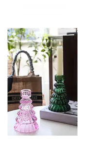 Détail de bougeoirs en verre rose et vert en forme de sapin sur table blanche