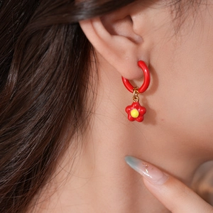 Close-up of red enamel flower drop earrings with golden hoops on a model's ear