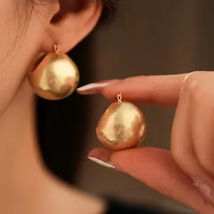 Minimalist gold textured spherical drop earrings with a matte metallic finish in macro view