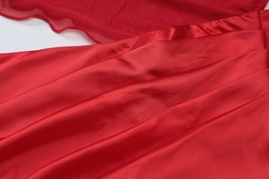 Detailed view of red satin fabric with sheer mesh wave trim and smooth texture