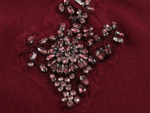 Intricate close-up of handmade floral beadwork and sequins on deep burgundy knit fabric