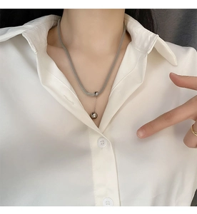 Dettaglio di una catena cubana in acciaio al titanio argento con ciondolo a sfera su modella