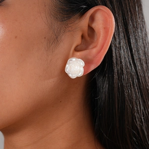 Detail shot of a white rose flower earring with pearl texture on a model's ear