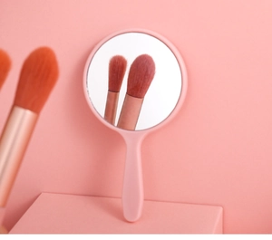 Detailed view of a pink handheld makeup mirror with an ergonomic handle and round glass