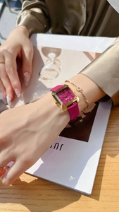 Macro shot of rectangular gold watch with magenta leather strap on woman's wrist