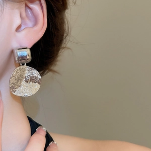 Detail of silver geometric drop earring featuring a textured circular pendant on model