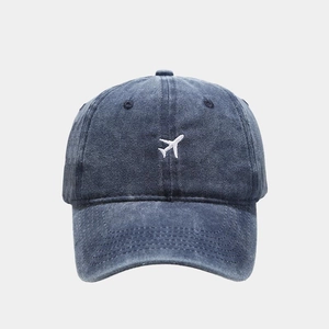 Close-up of small white airplane embroidery on a vintage navy blue denim baseball cap