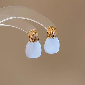 Dettaglio di orecchini dorati con eleganti pendenti a goccia in resina bianca e finitura
