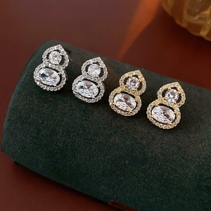 Detailed view of gold and silver gourd stud earrings with inlaid cubic zirconia on stand