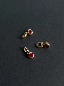 Macro shot of three gold pendants with vibrant red zircons on textured grey surface