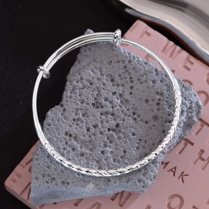 Polished silver adjustable hammered bangle with diamond-cut texture on dark volcanic rock