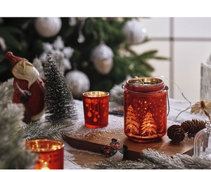 Detail of red Christmas glass candle holder with etched pine trees and warm glowing light