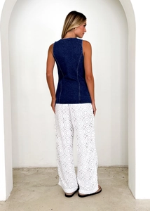 Detail view of denim vest back and white lace cut-out trousers in minimalist setting