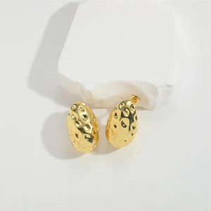 Golden oval stud earrings with hammered texture finish on white stone background