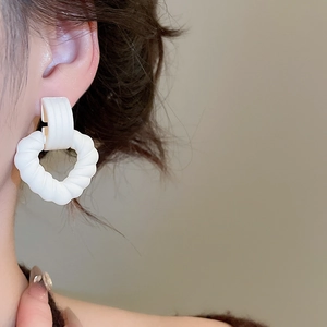 Close-up of white acrylic heart-shaped twisted earrings worn to show style and size