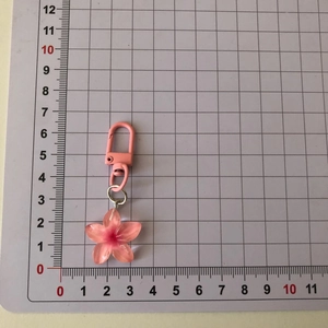 Pink translucent cherry blossom keychain measured on a grid cutting mat for size