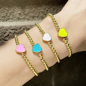 Detail of four gold beaded bracelets with colorful heart charms on a stone surface