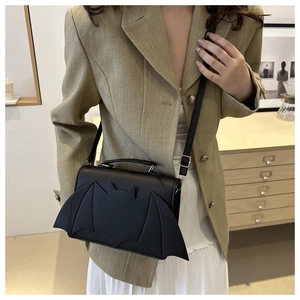Detail view of a black bat-shaped PU leather crossbody bag worn with a casual blazer