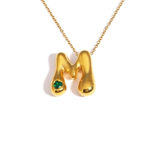 Detailed shot of 18k gold plated bubble letter M necklace with green heart gemstone
