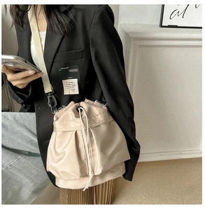 Detailweergave van de beige emmer tas met trekkoord en een brede geweven schouderriem