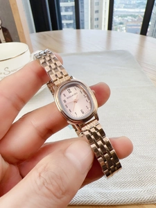 Close-up of rose gold oval quartz watch with metal link strap worn in natural light