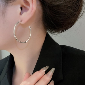 Side view of model wearing large minimalist polished silver hoop earrings with a black suit