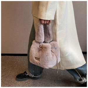 Model holding a dusty pink plush bucket bag with drawstring and metal nameplate
