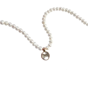 Baroque pearl necklace with round gold-rimmed clear pendant on a white background