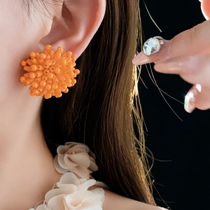 Close-up of bright orange 3D spherical firework stud earrings on a model's ear