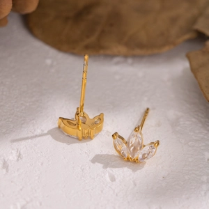Minimalist gold leaf stud earrings with marquise zircon stones on white texture background