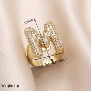 Detailed view of gold M letter ring with pavé zircons on silk background with dimensions