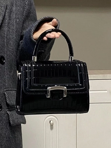 Close-up of black glossy crocodile texture handbag with silver D-ring buckle detail