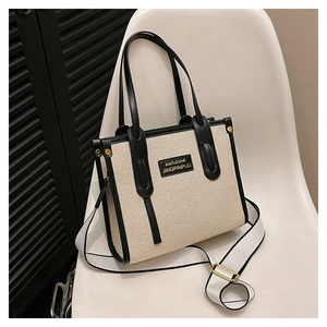 Detail of color-block canvas tote bag with wide strap and gold logo plate on white chair