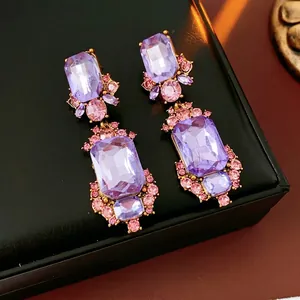 Vintage geometric drop earrings with purple crystals and gold settings on a black case
